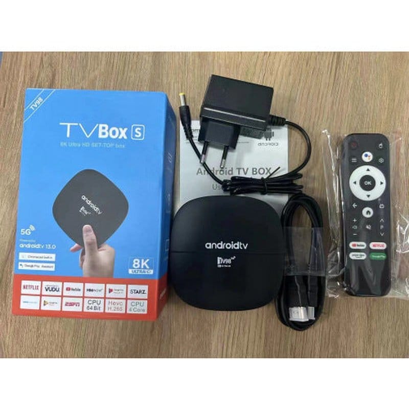 androidtv uređaj, adapter, kabl i daljinski upravljač na drvenoj podlozi pored kutije proizvoda