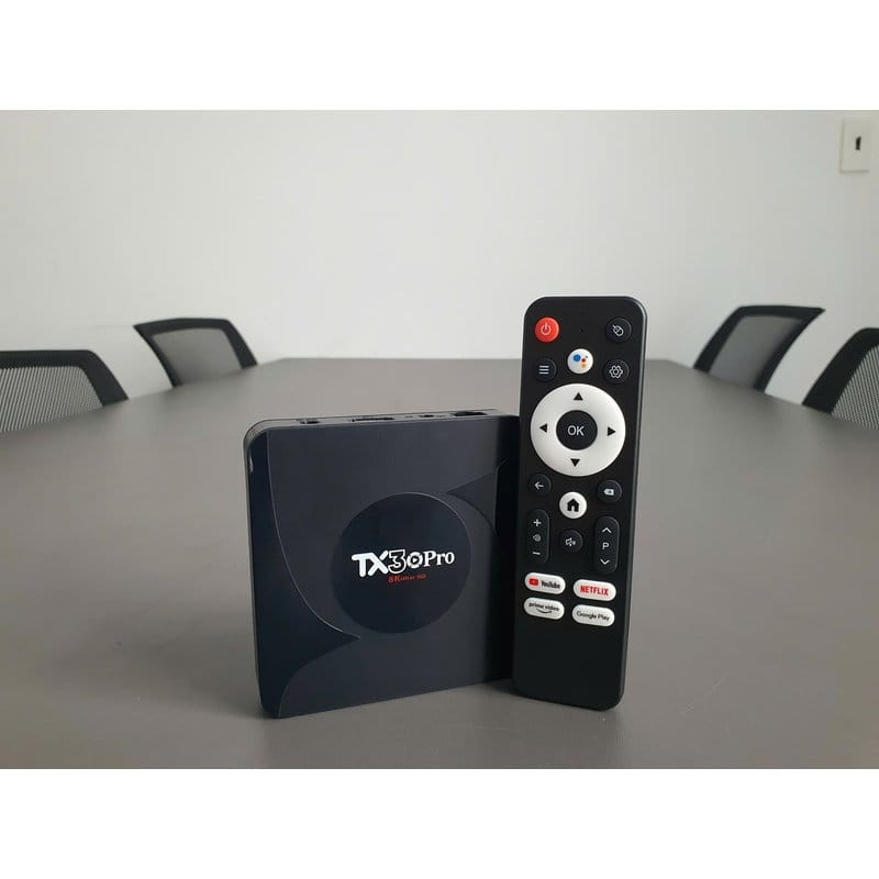android tv box tx30 pro i daljinski upravljač na stolu sa crnim stolicama u pozadini