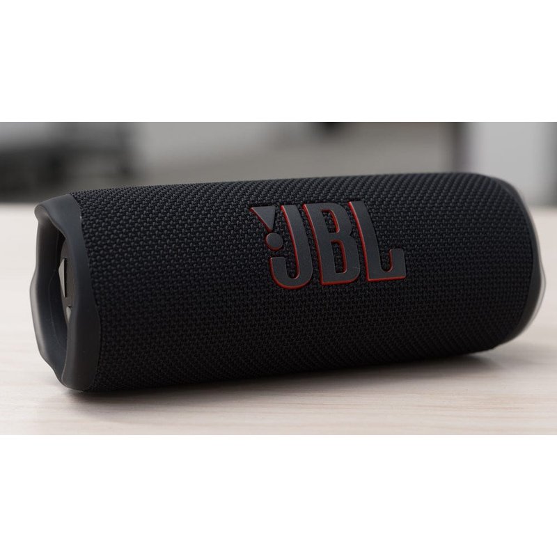 crni bluetooth zvučnik sa crvenim akcentima i ušicom za nošenje na stolu