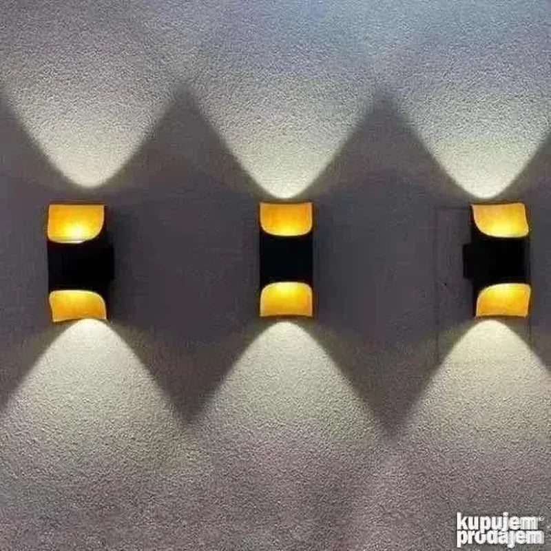 tri crne zidne lampe upaljene jedna pored druge na fasadi