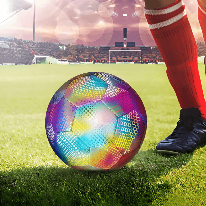 svetleća fudbalska lopta na terenu pored noge igrača u crvenim čarapama, stadion u pozadini