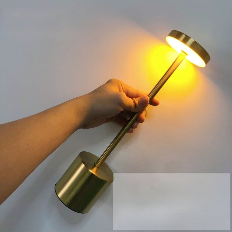 zlatna stona lampa u ruci osvetljava zid toplim žutim svetlom