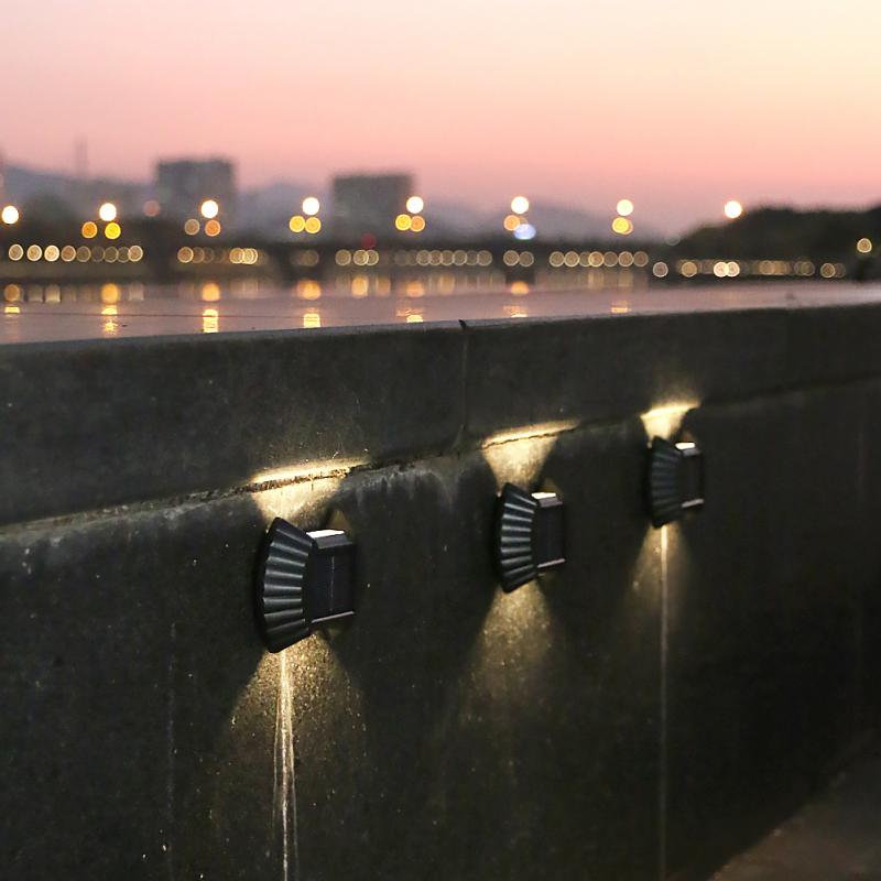tri solarne zidne lampe na betonskom zidu uz reku u sumrak, svetlo gore i dole